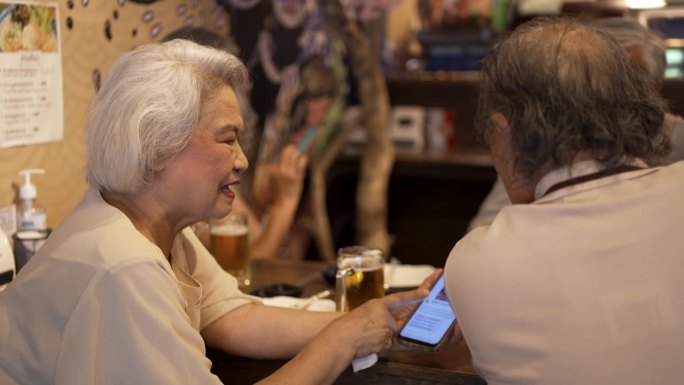 一群老年人在餐厅享用日本料理并玩智能手机。