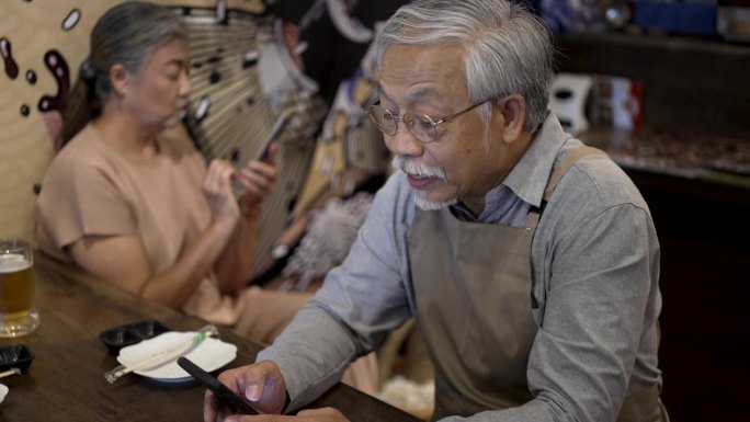 一群老年人在餐厅享用日本料理并玩智能手机。