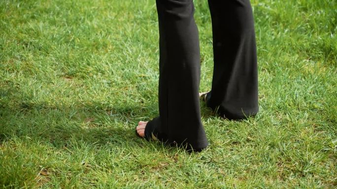 女性的腿在草地上随着流行音乐有节奏地舞动。女性的腿在草地上同步移动，随着时尚节拍摇摆。