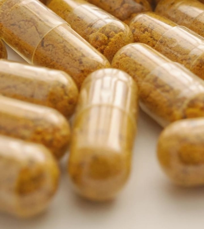 缓慢旋转的姜黄素胶囊，背景是医疗用品和药物的生产。制药行业：药物的生产与流通。创造健康的过程：营养补