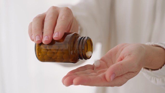特写镜头：女性手从棕色瓶子中倒出白色药丸。暗示医疗、药物或补充剂，强调日常健康习惯和个人护理。女性健