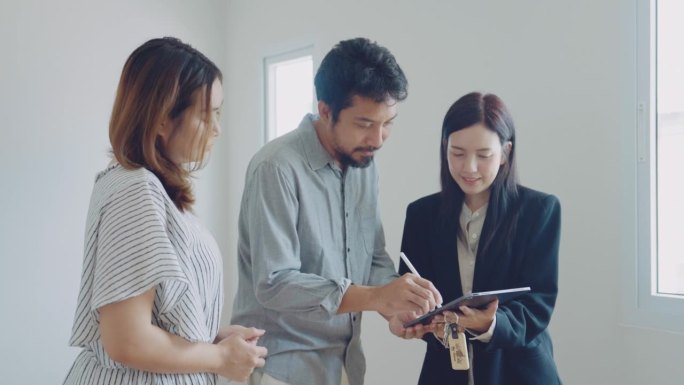 年轻的亚洲夫妇在数字平板上签署贷款批准书。