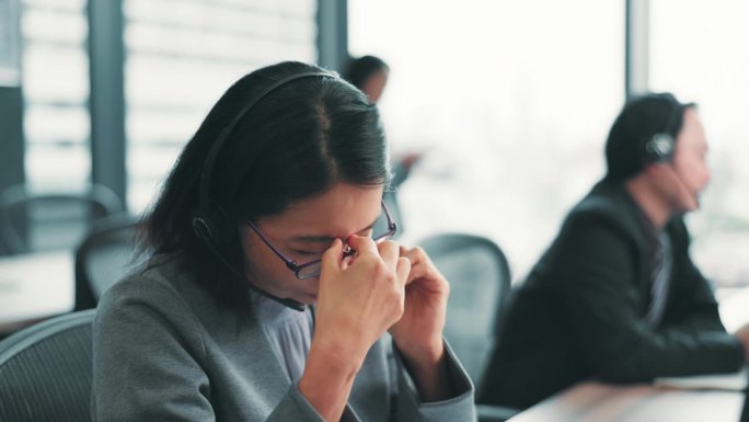 沮丧的亚洲女性或客服代理在呼叫中心因压力、焦虑或疲劳而感到头痛。日本女性或顾问佩戴耳机，因疲惫或眩晕