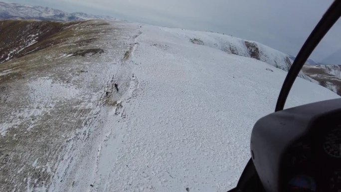 低空高速山顶飞越直升机驾驶舱视角，人们在冬季寒冷的雪地上徒步旅行和滑雪。