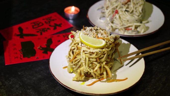 中国新年。亚洲美食，包括虾和肉类的面条菜肴。节日的家庭晚餐。红色背景上的金币、扇子和带有象形文字的卡