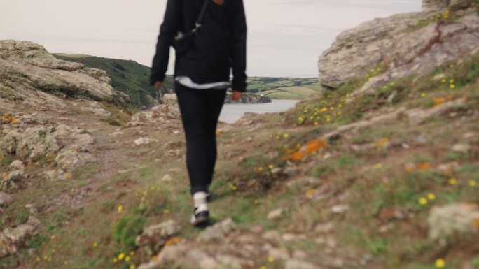 女人沿着小径徒步旅行，远处可以看到大海的景色。