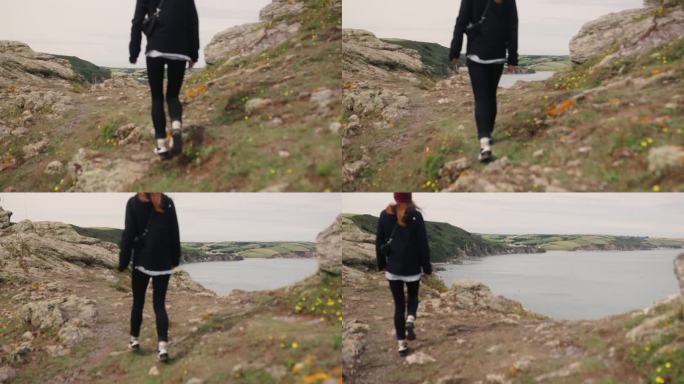 女人沿着小径徒步旅行，远处可以看到大海的景色。