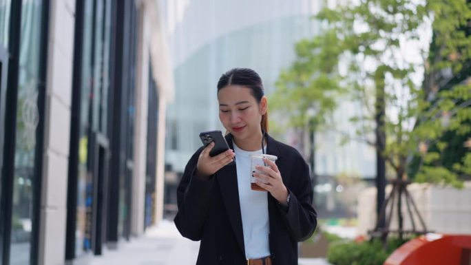 女性在现代办公室外放松，走动并使用智能手机，享受咖啡休息时间。