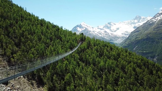 无人机飞离查尔斯·库奥嫩悬索桥（Hängebrücke），背景是瑞士瓦莱州兰达的雪山。