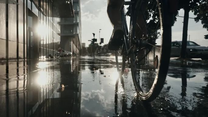 在日落时分，轻微降雨中，女人骑自行车在湿滑的城市人行道上的表面镜头。