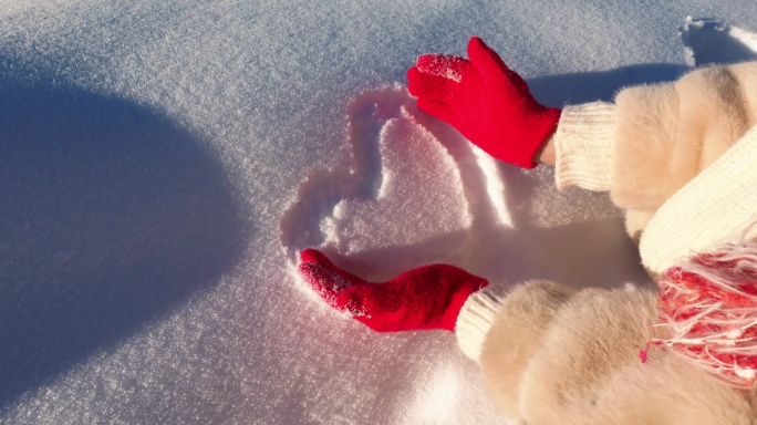 戴红手套的手在雪上画心形
