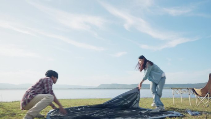 一男一女正在湖边的草地上搭帐篷。