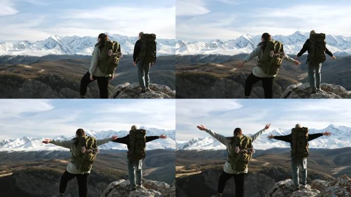 背影两位背包女 hikers，举起手站在高山上。