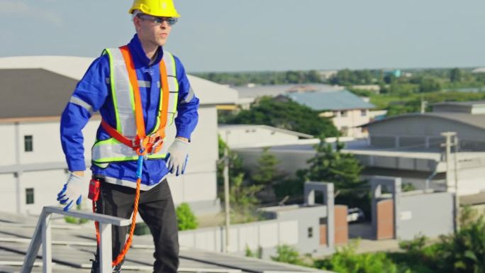 年轻的技术工人从楼梯上走到屋顶上，用日光检查和维护建筑物或工厂的太阳能电池板。