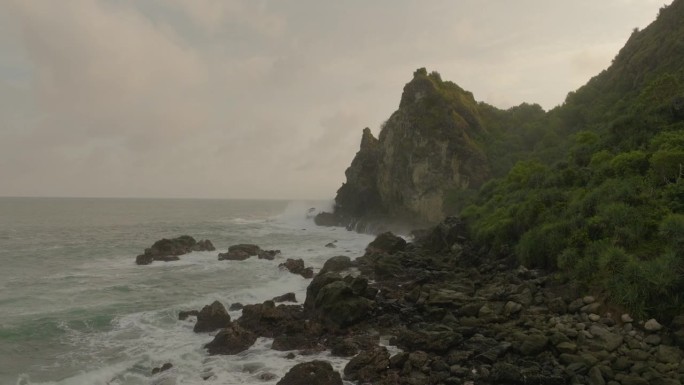 空中向前上升的镜头，如果田园诗般的镜头，大海溅在山上对多云的天空-爪哇，印度尼西亚