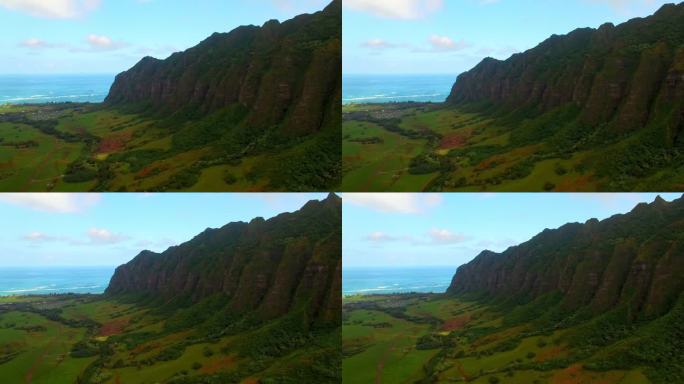 在夏威夷瓦胡岛，无人机在绿色景观上向后飞行，航拍的靠近大海的山与蓝天