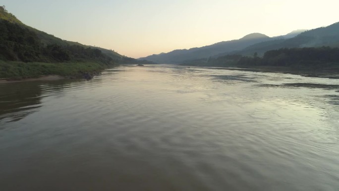 空中拍摄的河流在山中对天空日落，无人机飞向前在森林中的树木涟漪的水-湄公河，老挝