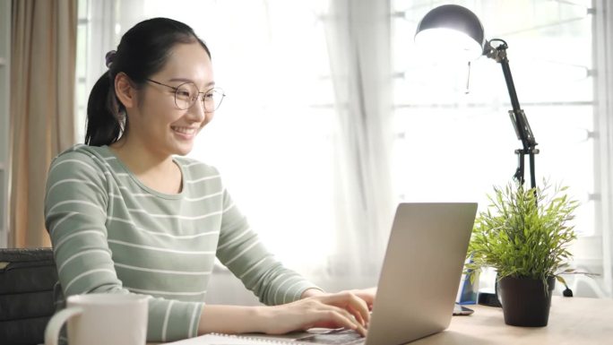 认真的女生戴着耳机在线学习与网络老师学习语言谈话看着笔记本电脑，专注的年轻女生做视频电话辅导写笔记，