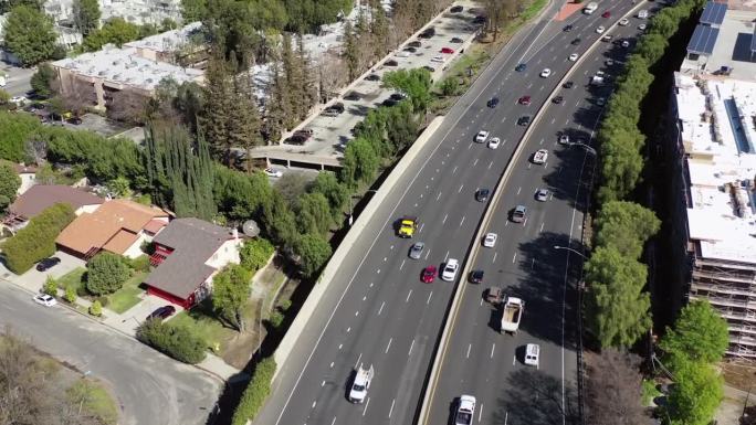 航拍:阳光明媚的一天，无人机拍摄在城市高楼之间的高架道路上的车辆——加州的伍德兰山