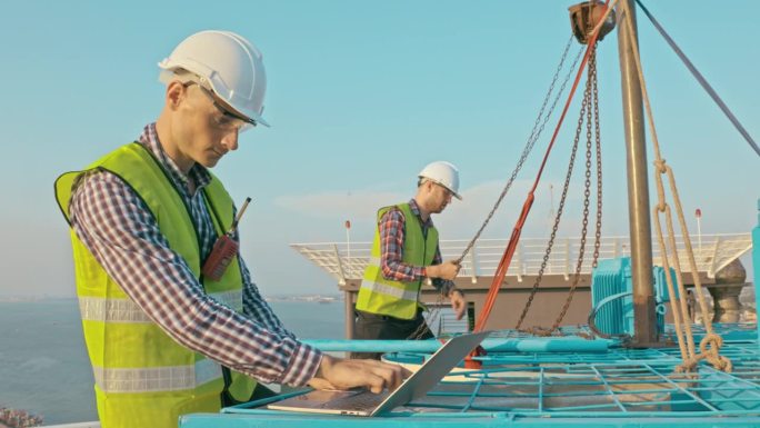 两名维修工正在对大型工业建筑的冷却塔空调和水冷却塔空调系统进行机械工作，以确保设施空调系统的最佳性能