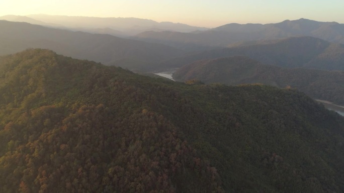 空中拍摄的绿树在山上的森林日落，无人机飞向河流对天空-湄公河，老挝