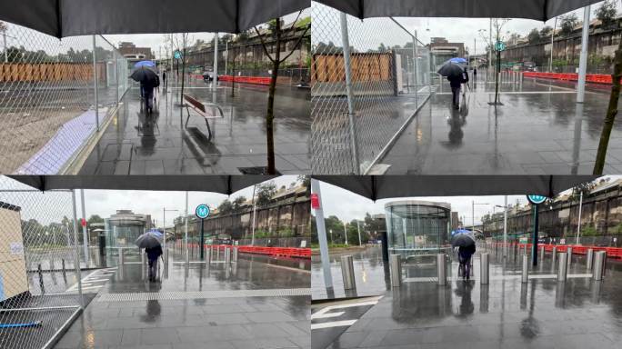 一个男人在雨中走向正在建设中的Barangaroo地铁站，手里撑着伞，右边是围栏，左边是空旷的工地。