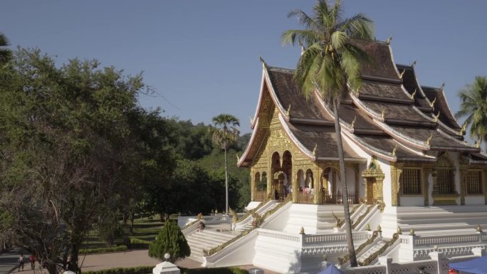 在阳光明媚的日子里，游客在著名的Phra Bang寺庙中对着天空的树木-琅法邦，老挝