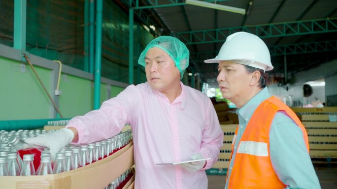 在饮料出厂前，饮料厂的工人团队检查饮料货架上的瓶子的清洁度。