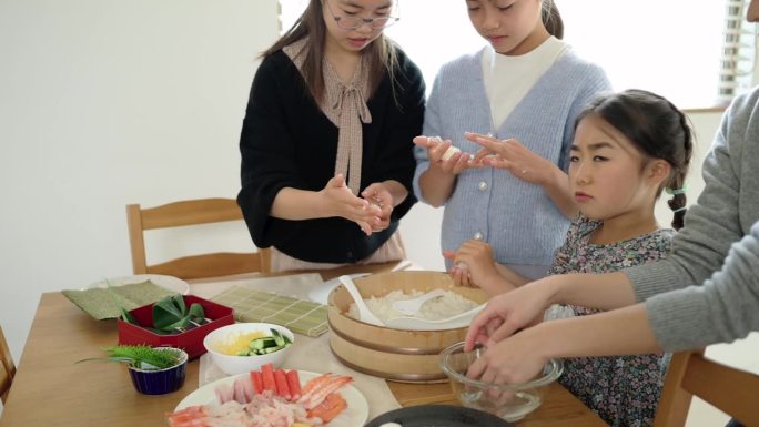 三个日本女孩和她们的母亲正在卷醋饭做寿司。