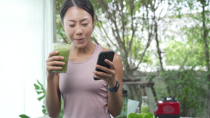 年轻微笑的女人用吸管喝着排毒冰沙。快乐的素食者喝新鲜的绿色蔬菜鸡尾酒。