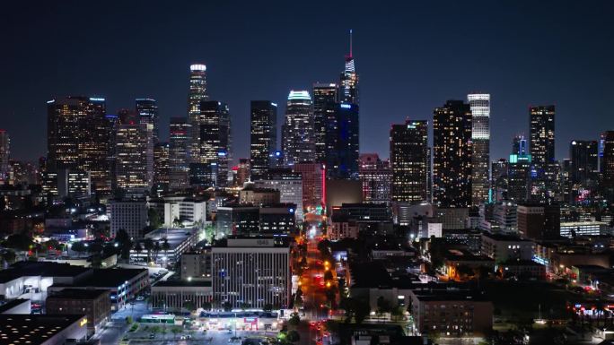 无人机镜头向前飞行并下降至洛杉矶市中心摩天大楼的夜景。