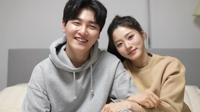 家——年轻的女人和男人在床上看着照相机，在卧室里挽着他们的胳膊