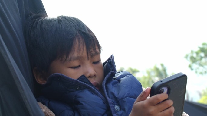 穿着羽绒服的小孩在户外放松，专注于手机。