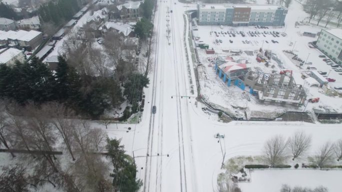 无人机镜头展示了一条被雪覆盖的道路，路上有经过的汽车，镜头向上升起，进入一条延伸的多云道路。