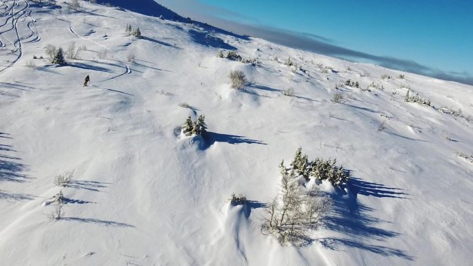 无人机镜头拍摄一名男滑雪者在美丽晴朗的日子里滑下山坡。