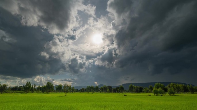 乌云聚集在郁郁葱葱的绿地上，预示着暴风雨的来临，零星的阳光透过云层洒下。