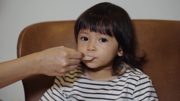 母亲用勺子给生病的幼儿喂液体药物。