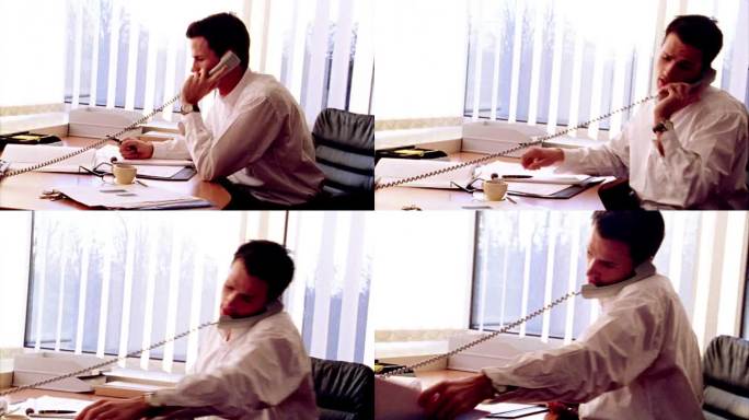 过度曝光的摄影车拍摄了商人在电话上谈话+查看桌子上的文件在办公室/窗户的背景