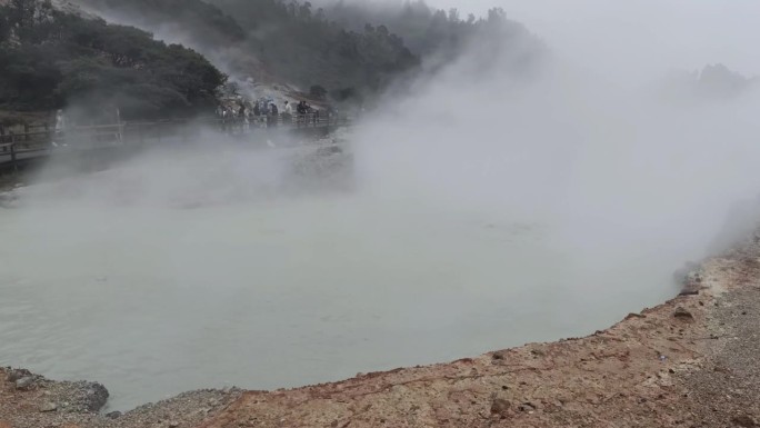 火山口全景，里面充满了热硫，冒出大量刺鼻的蒸汽，周围是坚固的岩石，许多游客在游览。