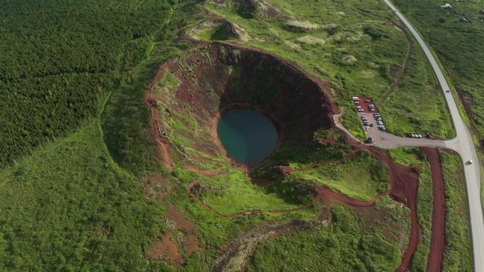 冰岛凯里德火山口的鸟瞰图，展示了其引人注目的蓝色湖泊、红色火山岩、绿色坡地和步道。