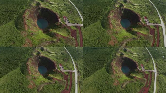 冰岛凯里德火山口的鸟瞰图，展示了其引人注目的蓝色湖泊、红色火山岩、绿色坡地和步道。