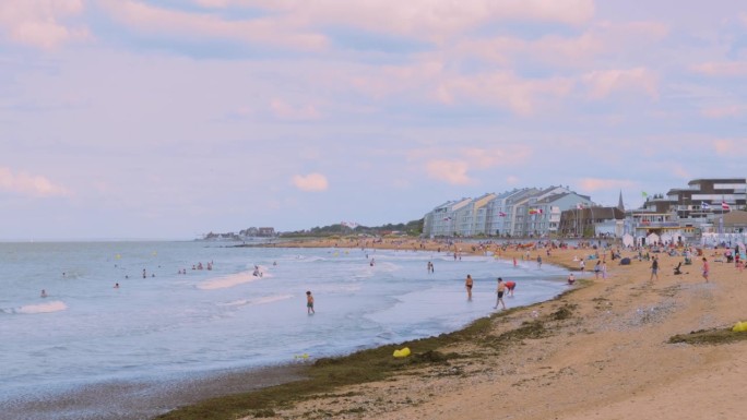 历史悠久的二战诺曼底D日朱诺海滩，数百名海滩度假者在和平时期晒太阳或在海中游泳，4K。