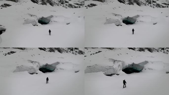 滑雪者从空中视角进入一个冰冻的冰川洞穴，探索瑞士瓦莱州一个偏远的阿尔卑斯山谷，天气阴云密布的冬日。