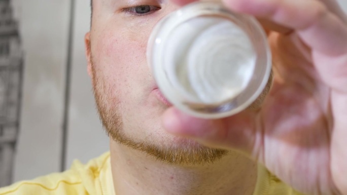 特写镜头：一名男子美味地从透明玻璃杯中饮用新鲜牛奶。男子饮用酸奶或乳制品的肖像。为身体补充钙质储备。