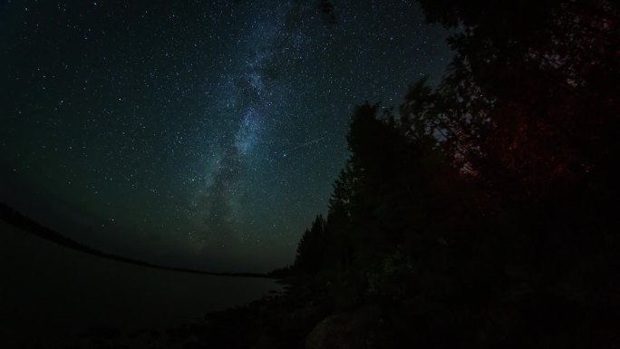星空延时摄影，灌木丛中的篝火，森林后方的北极光或极光。