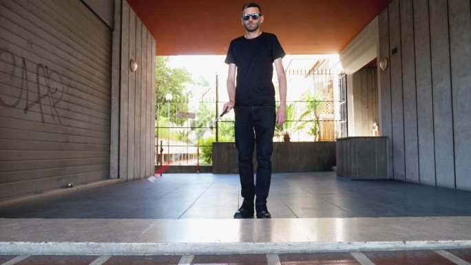 一个坚定的盲人，靠着手杖自信地走近并跨过他面前的台阶，展示了他在周围世界中导航的韧性和适应能力。