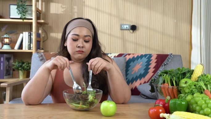 一个面露烦恼表情的超重女性手持一把新鲜生菜的叉子。