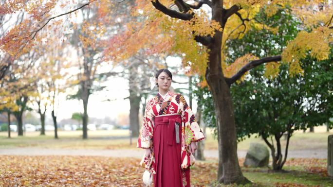 一位20多岁的年轻女性穿着日本传统的毕业典礼袴（和服），在一座传统日本房屋前的美丽地方漫步。