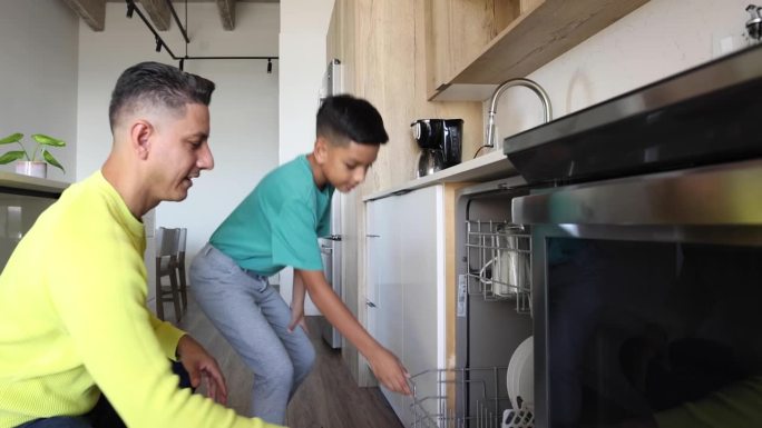 一位拉丁裔父亲和他的小儿子穿着休闲服装，把碗碟放进洗碗机里。