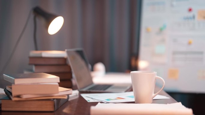 摇臂镜头拍摄的工作桌，桌上满是纸质文件、图表、笔记本电脑和台灯，背景是家中工作室的深夜场景。